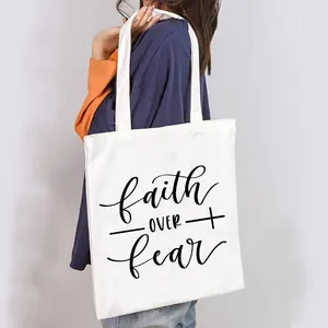 Detailed view of white canvas tote bag with 'Faith Over Fear' print on a model