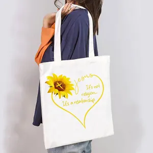 Detailed view of women's white canvas tote bag with sunflower design carried by a model