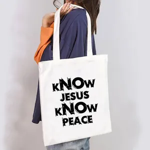 Close-up detail of a white canvas tote bag with black KNOW JESUS KNOW PEACE quote print