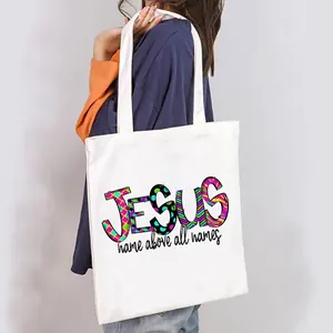 Casual white canvas tote bag featuring a colorful JESUS print, shown carried over the shoulder.