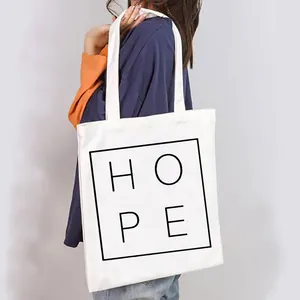 Close-up of a white canvas tote bag with 'HOPE' print carried by a model.