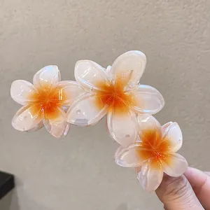 Vue détaillée de trois fleurs de frangipanier sur une pince à cheveux orange translucide