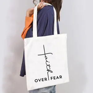 Detail view of a white canvas tote bag with Faith Over Fear print carried by a model