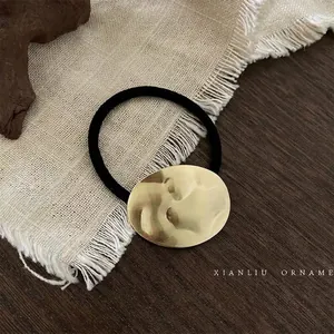 Close-up of a minimalist gold brushed metal oval ornament on a black hair tie.