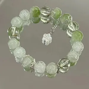 Close-up of a green and white beaded bracelet with a flower charm on a mirrored surface