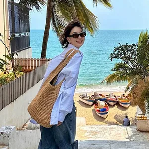 Große geflochtene Strohtasche für den Strandurlaub von einem Model am Meer getragen