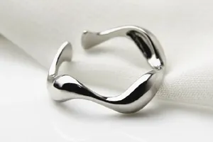 Detailaufnahme eines minimalistischen silbernen wellenförmigen offenen Rings mit glatter Oberfläche