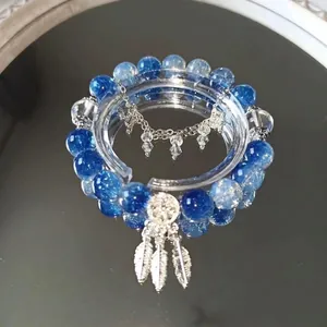 Close-up detail of a handcrafted blue beaded bracelet with silver dreamcatcher and feather charms