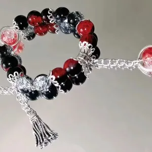 Macro detail of red and black beaded bracelet with silver tassel pendant on mirror.