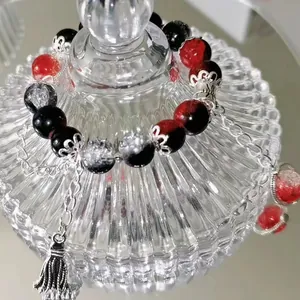 Detailed close-up of a red and black beaded bracelet with a silver tassel charm on glass