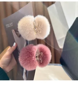 Close-up of plush fur ball hair clips in pink and beige with clear claw grips.