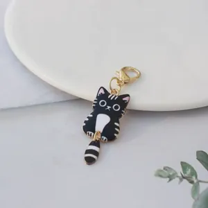 Close-up view of a cute black and white cartoon cat keychain with a gold clasp