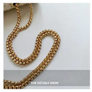 Macro detail of a shiny gold-toned box chain shoulder strap for a fashion handbag