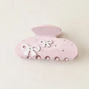 Detailed view of a pink acetate hair claw clip with elegant 3D white bows and rhinestones