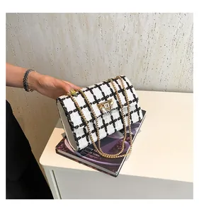 Chic black and white checkered chain bag held over a magazine on table.