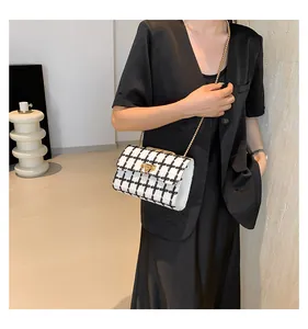 Detail view of black and white plaid chain bag on a model in a black outfit.