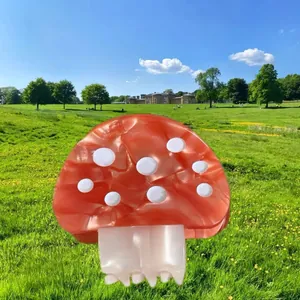 Vista dettagliata di un grazioso fermaglio a fungo in acetato rosso e bianco in un prato verde