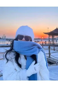 Atmospheric lifestyle shot showing a thick light blue scarf worn in a snowy sunset setting.