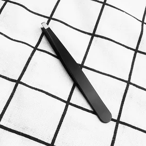 Detail of black slant-tip eyebrow tweezers placed on a black and white grid cloth
