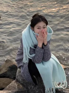 Asian model wearing a thick light blue fringe scarf in an atmospheric seaside autumn setting