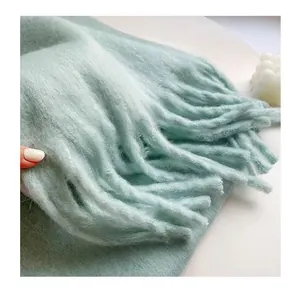 Close-up detail of thick tassels and soft plush texture on a mint green winter scarf