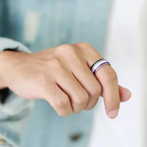 Detail of 8mm asexual pride flag stripe ring on finger with denim jacket background.
