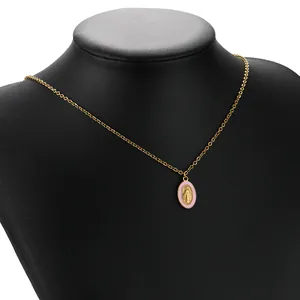 Close-up detail of a gold Virgin Mary pendant necklace with pink enamel on a black mannequin.