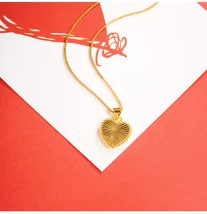 Close-up of a gold heart pendant with sunburst texture and beaded edge on a box chain