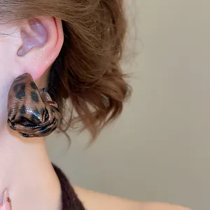 Detailed view of fashionable leopard print leather rose earrings on a model's ear