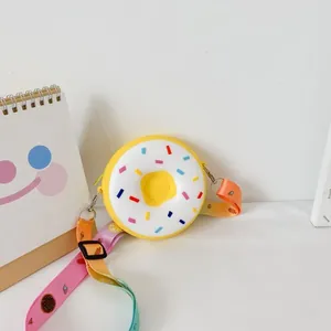 Yellow donut-shaped silicone crossbody bag for children with rainbow patterned strap.