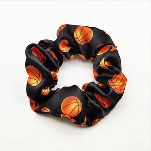 Detail view of black satin hair scrunchie featuring a vibrant orange basketball pattern print.