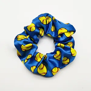 Close-up detail of a blue satin hair scrunchie featuring a vibrant yellow softball pattern