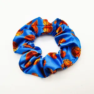 Detailed view of a vibrant blue satin hair scrunchie featuring orange basketball prints