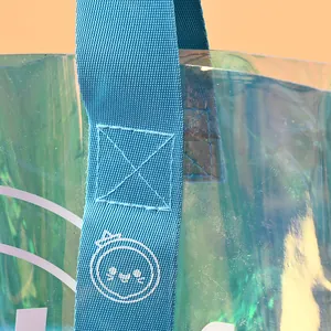 Close-up of iridescent PVC tote bag with blue woven handle and cute cartoon logo