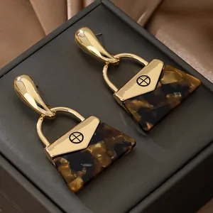 Vue détaillée de boucles d'oreilles pendantes dorées en forme de sac à main chic.