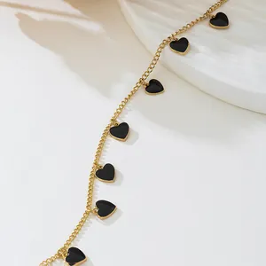 Vue détaillée d'un collier en chaîne dorée avec des pendentifs cœurs noirs sur fond blanc