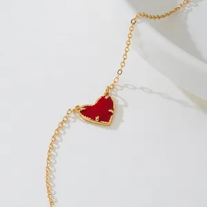 Vue détaillée d'un élégant collier en chaîne dorée avec un pendentif cœur rouge vif.