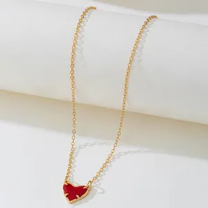 Gros plan d'un collier en chaîne dorée avec pendentif cœur rouge sur support blanc.