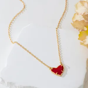 Gros plan détaillé d'un collier en chaîne dorée avec un pendentif cœur en émail rouge vif.