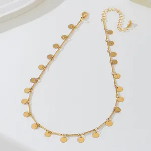 Détail d'un collier en chaîne dorée avec de multiples petits charms en forme de disque rond.