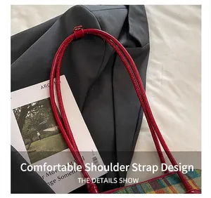 Detailed macro view of the thin red tubular shoulder strap on a plaid fabric bag.