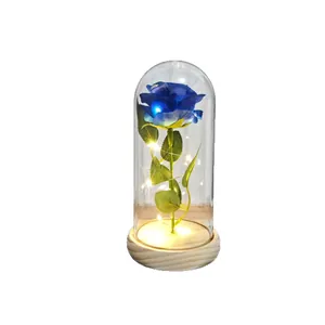 Blue artificial rose in glass dome with warm LED fairy lights on wooden base