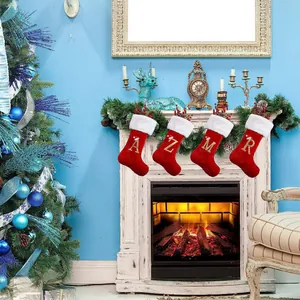 Large red Christmas stockings with gold embroidered letters hanging on a cozy fireplace