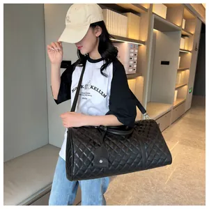 Black quilted travel duffel bag shown on model with adjustable shoulder strap and handles.