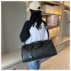 Large black quilted travel duffel bag with shoulder strap shown in a room.