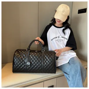 Large black quilted travel duffel bag being held by a model in an indoor lounge