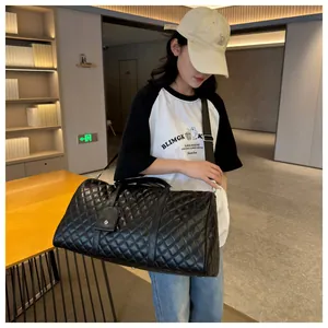 Model carrying a black diamond-quilted travel duffel bag with a shoulder strap