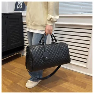 Close-up of a stylish black quilted travel duffel bag held by a person indoors.