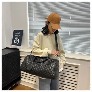 A stylish woman carrying a large black quilted duffel travel bag in an indoor setting