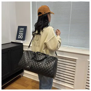 Female model carrying a large black quilted diamond lattice travel duffel bag indoors